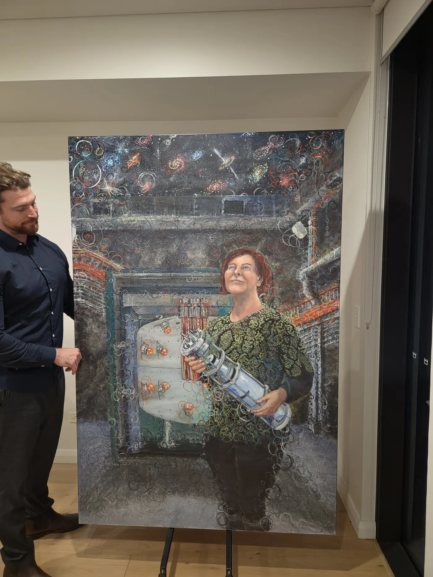 The Observer of Dark Matter hung on a gallery wall with the artist standing beside it for scale